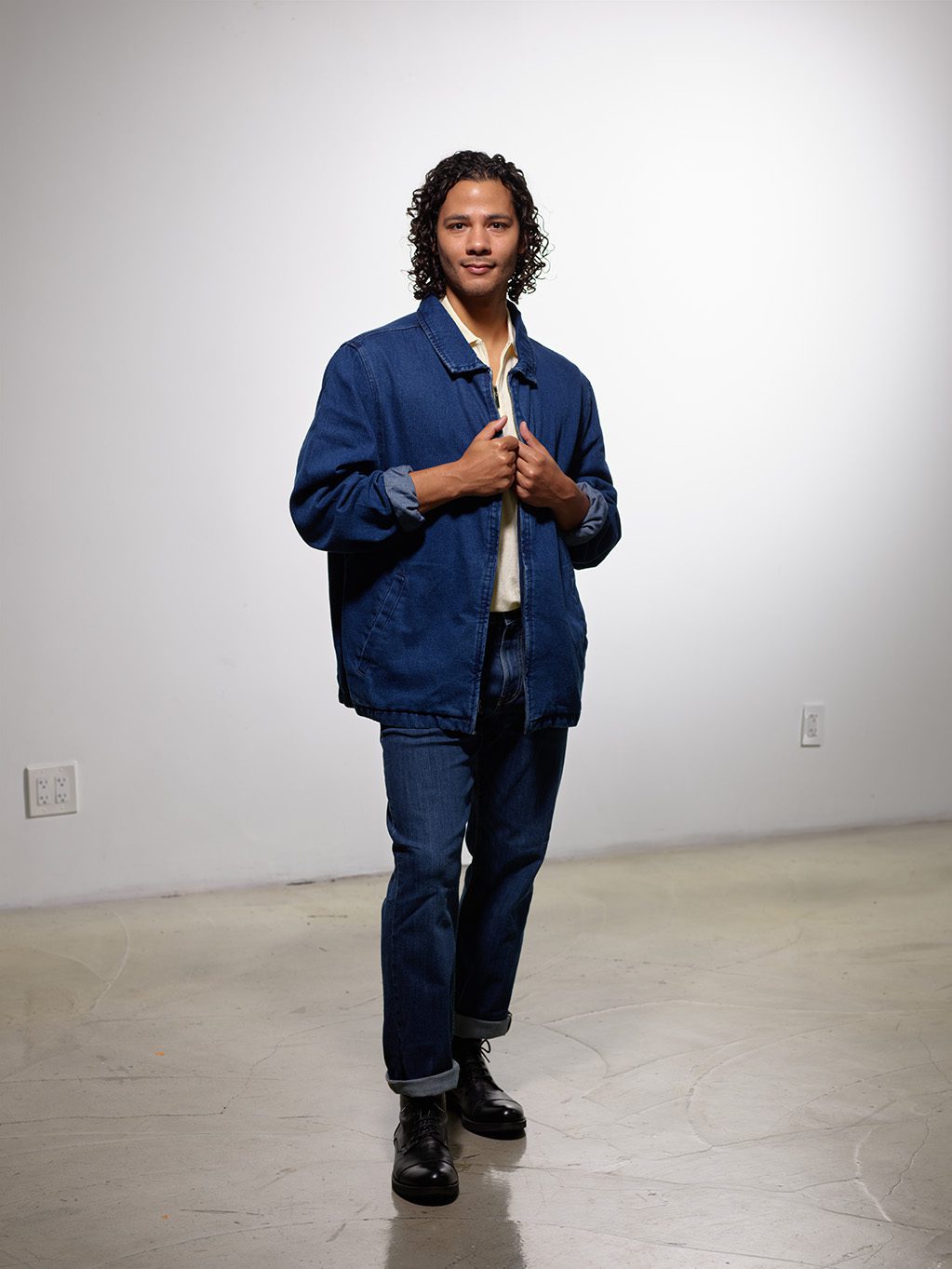 Joseph A. Hernandez poses for the camera with a slight smile. He is a brown-skinned man with medium-length curly brown hair and brown eyes. He is wearing a denim overshirt over a white shirt with blue jeans.