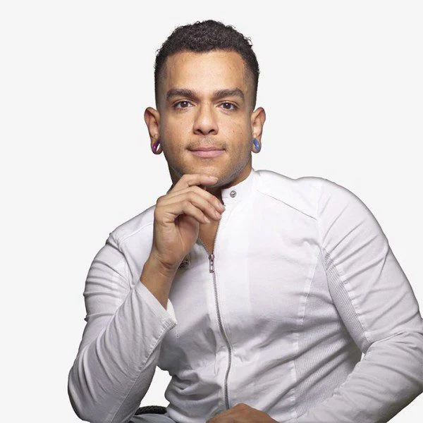 2023AXIS_JanpiStar_byDavidSilva_Square JanpiStar poses for the camera. They are a Latinx wheelchair user with light brown skin and long arms. They are wearing a a white athletic top.