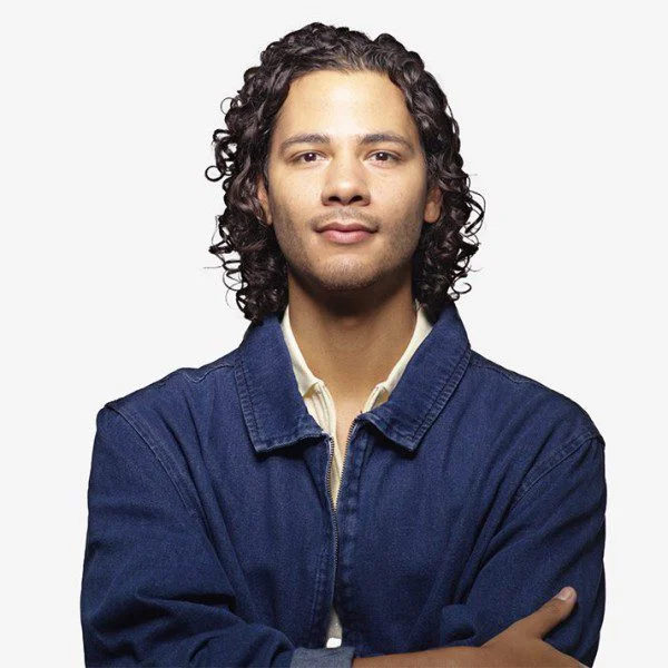 2023AXIS_JosephHernandez_byDavidSilva_Square Joseph A. Hernandez poses for the camera with a slight smile. He is a brown-skinned man with medium-length curly brown hair and brown eyes. He is wearing a denim overshirt over a white shirt.