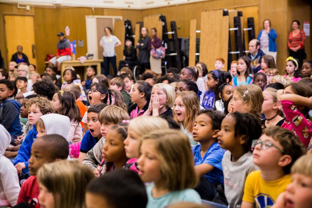 Children have expressions of shock on their faces as they watch AXIS perform during an assembly. 