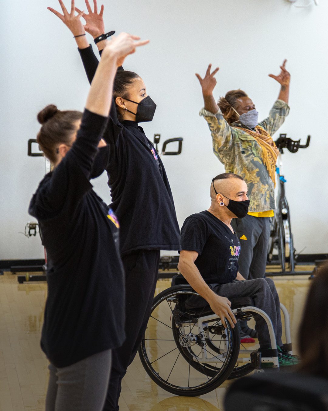 Three disabled and non-disabled AXIS dancers and a class participant raise their hands upwards together with feeling.