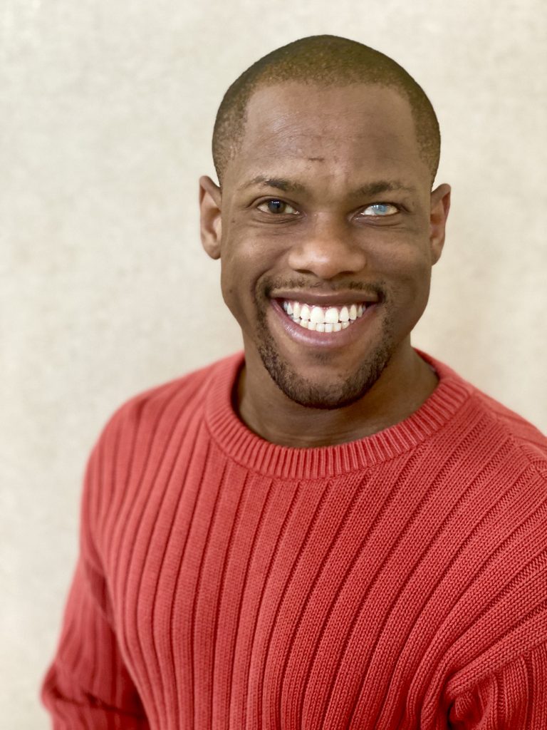 Photo of Davian Robinson in orange sweater with a big wide smile.