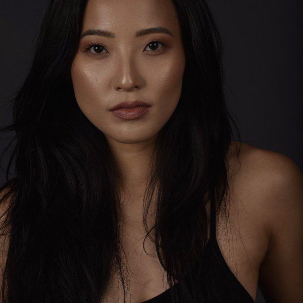 A headshot of Julie, a woman of Japanese descent from Brazil. She has long black hair and wears a black tank top.