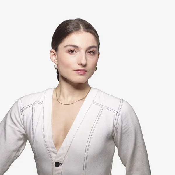 2023AXIS_AnnaGichan_byDavidSilva_Square Anna, a young white woman in a white jumpsuit, smiles warmly at the camera.