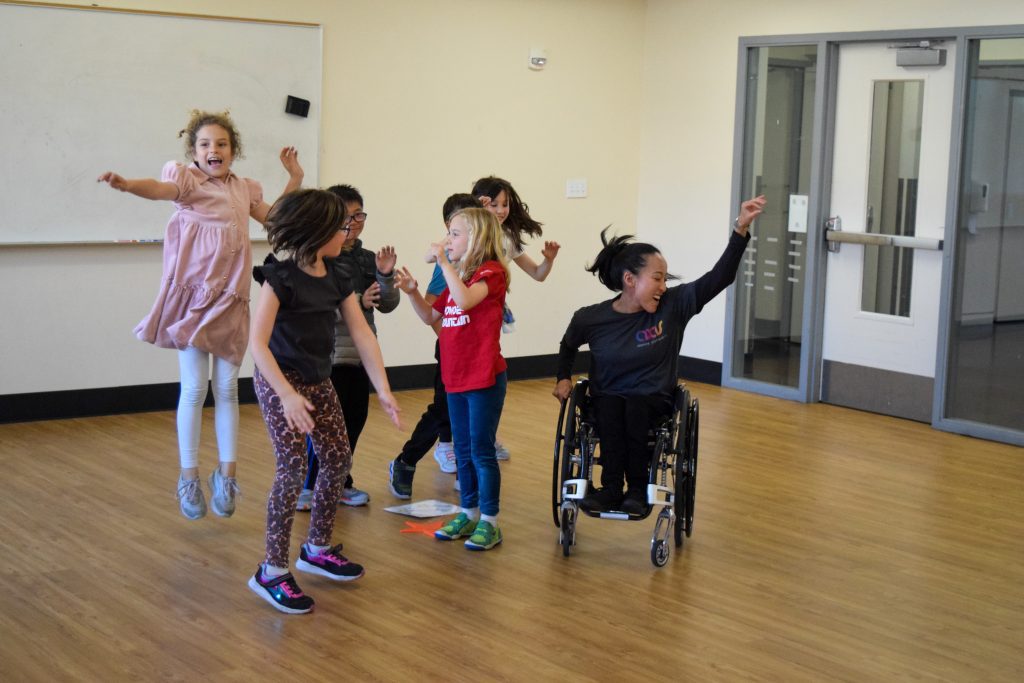AXIS Dancer Julie Hasushi, who is a wheelchair user, dancers with young children in a workshop