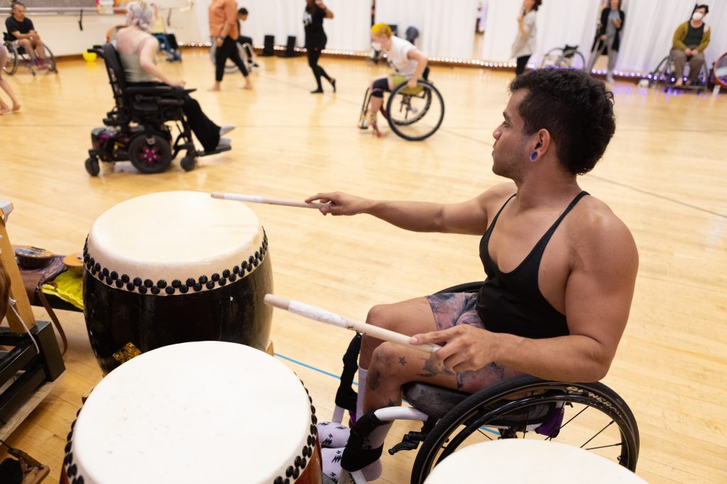AXIS dancer JanpiStar plays the drums as other disabled and non-disabled dancers improvise behind them.