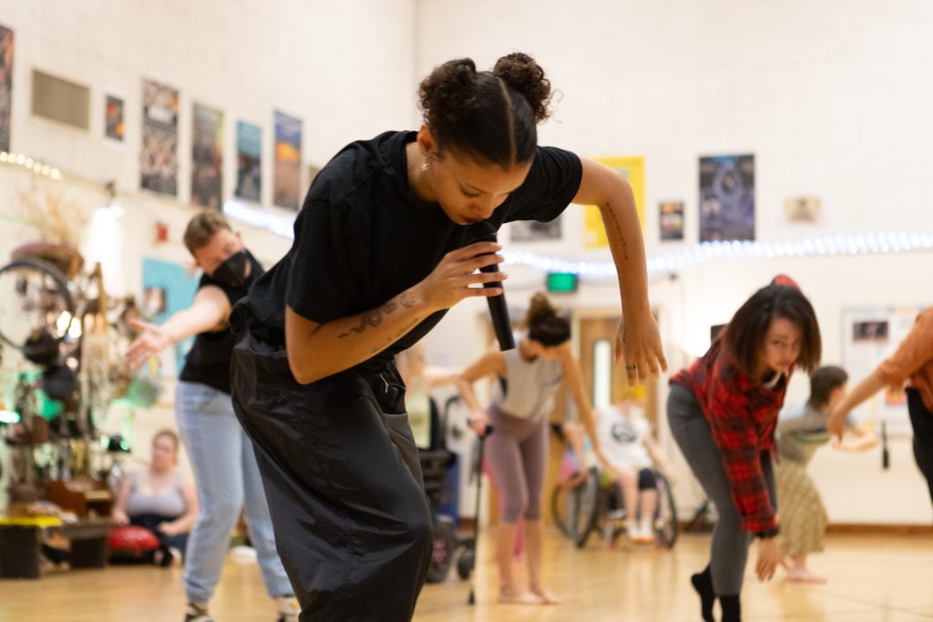Alaja Badalich holds a microphone and instructs Summer Intensive participants who follow along behind her.