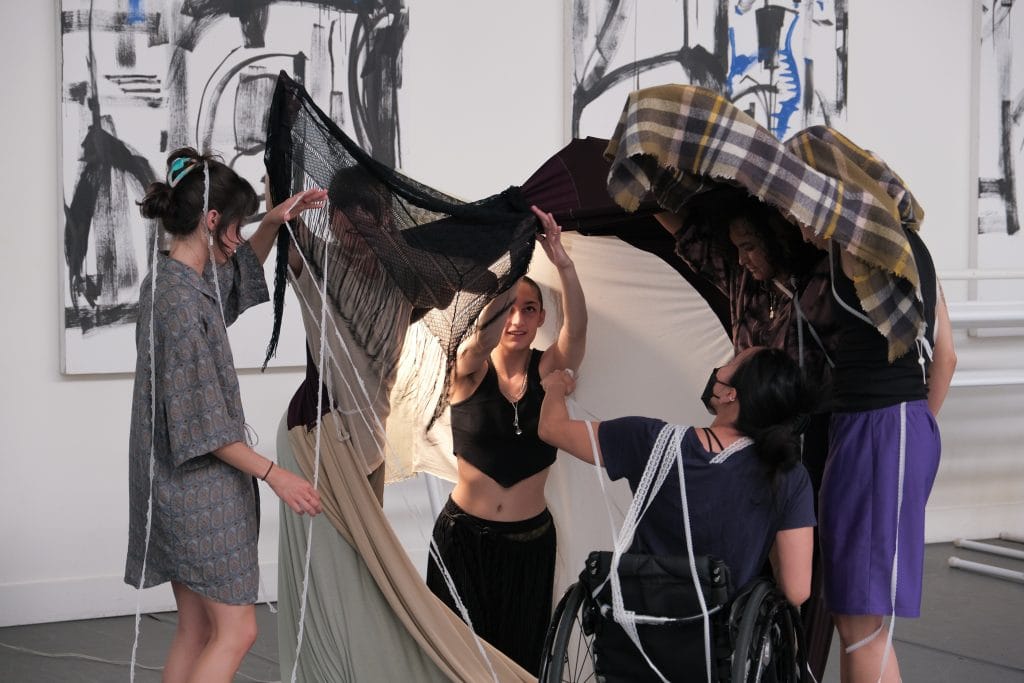 Five dancers improvise in a fort-style textile installation. At the center, choreographer August looks up with wonder.