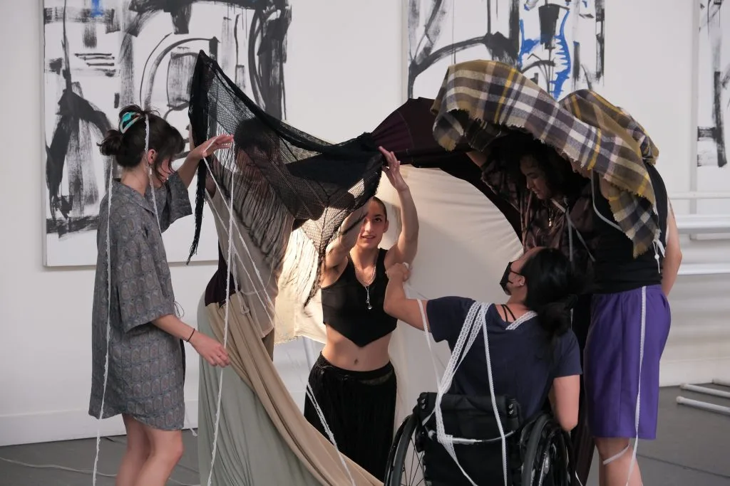 Five dancers improvise in a fort-style textile installation. At the center, choreographer August looks up with wonder.