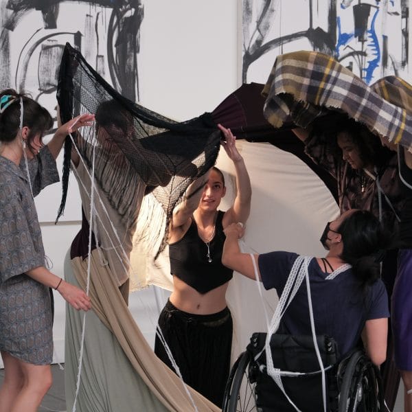 Five dancers improvise in a fort-style textile installation. At the center, choreographer August looks up with wonder.