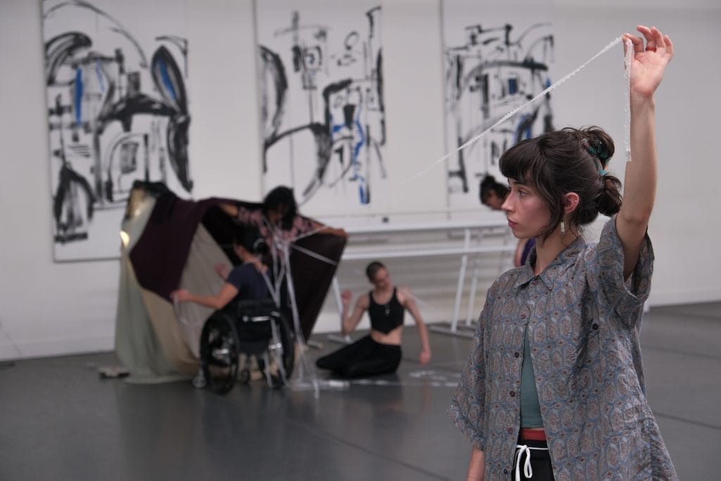 In the foreground, AXIS Apprentice Clairey pulls a string of lace away from the center of a fort-like textile installation in the background.