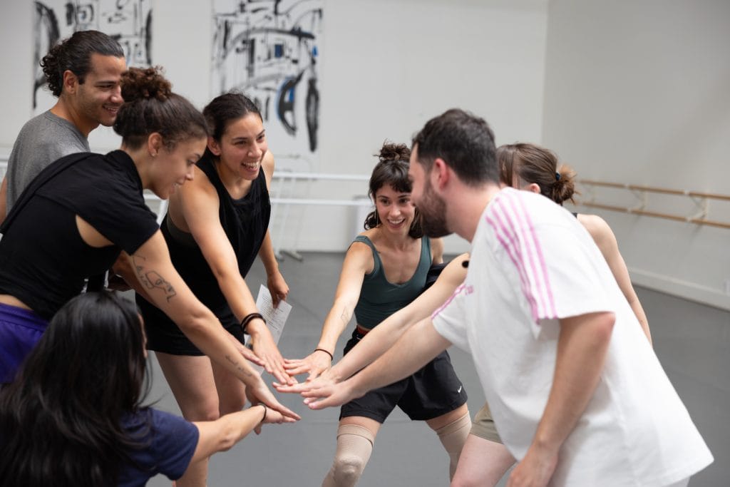 Choreographer Brian and the AXIS team put their hands together in a circle, all smiling