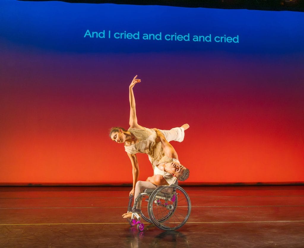 JanpiStar leans their torso to one side in their wheelchair, as Zara does an arabesque with one hand on the chair for support and stability. Against an orange - blue gradient, subtitles read "And I cried and cried and cried."