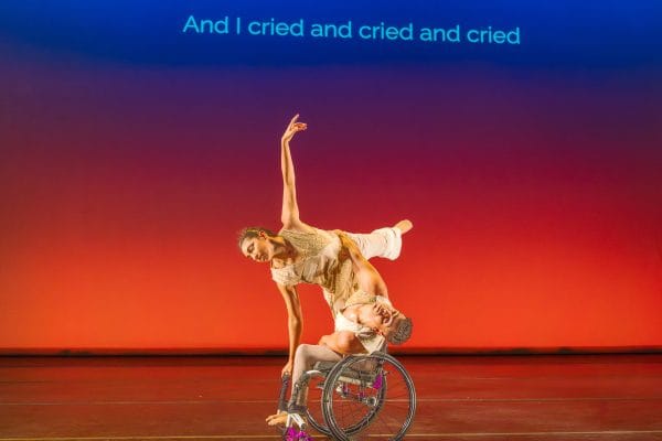 JanpiStar leans their torso to one side in their wheelchair, as Zara does an arabesque with one hand on the chair for support and stability. Against an orange - blue gradient, subtitles read "And I cried and cried and cried."