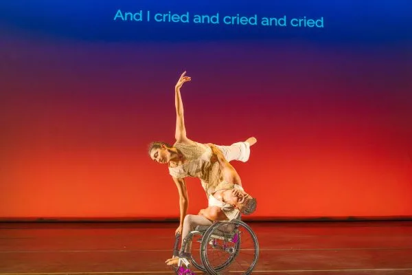 JanpiStar leans their torso to one side in their wheelchair, as Zara does an arabesque with one hand on the chair for support and stability. Against an orange - blue gradient, subtitles read "And I cried and cried and cried."