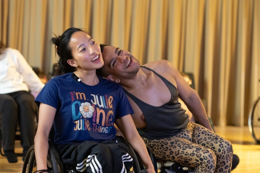 AXIS Dancers Julie & JanpiStar, who are both wheelchair users, smile and laugh as they lean onto each other's shoulders.