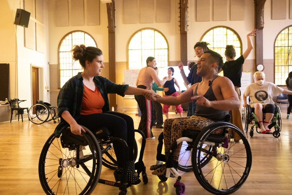 AXIS Dancer & Teaching Artist JanpiStar, who is a wheelchair user, teaching Salsa to an adult student using a wheelchair.