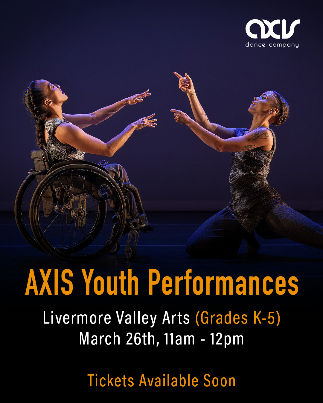 AXIS dancers Julie and Alaja point two fingers at each other and smile while performing on stage. Julie uses a wheelchair and Alaja crouches down; both dancers wear silvery costumes reminiscent of moonscapes.