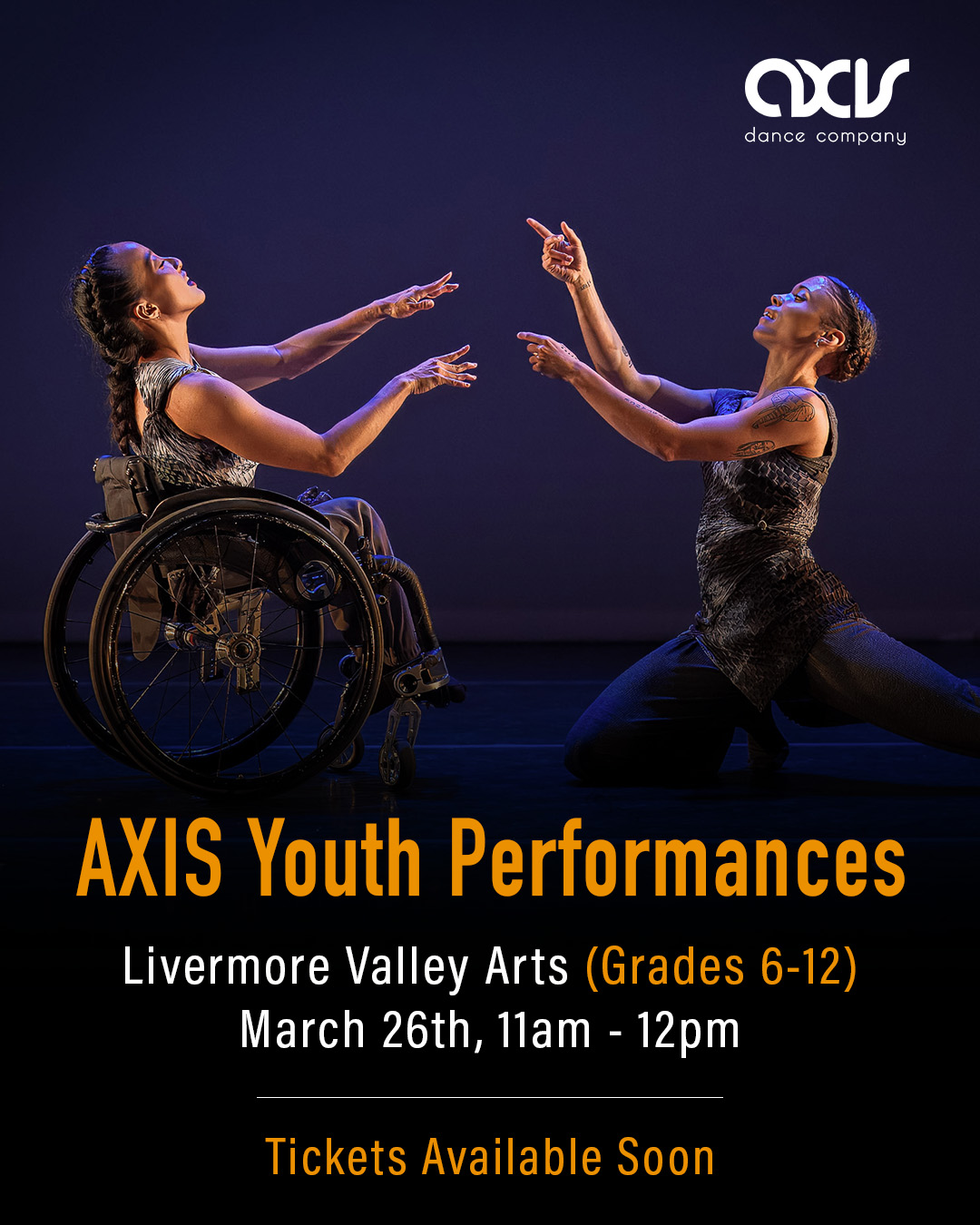 AXIS dancers Julie and Alaja point two fingers at each other and smile while performing on stage. Julie uses a wheelchair and Alaja crouches down; both dancers wear silvery costumes reminiscent of moonscapes